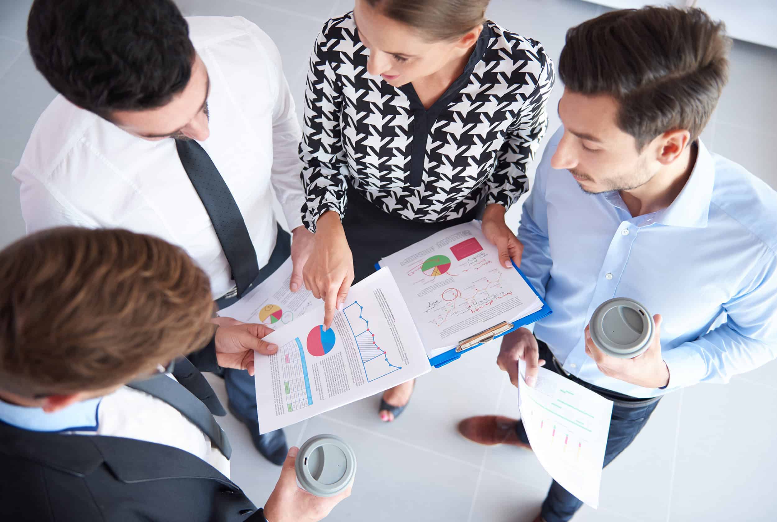 Four employees discussing over printed reports with tables and graphs.