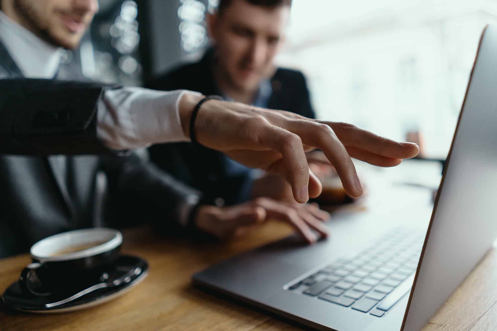 Two men are discussing something on a laptop over coffee.