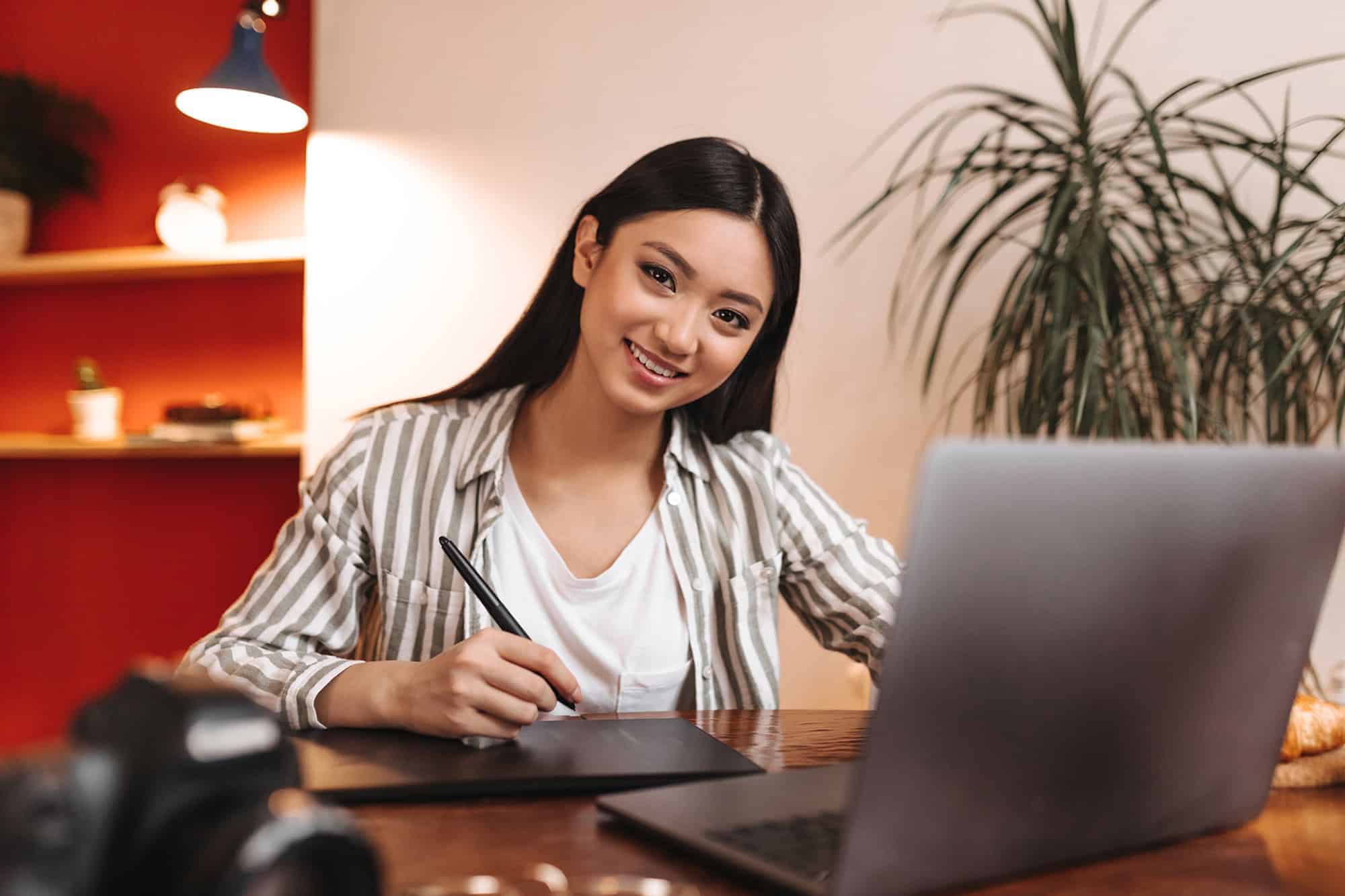 A smiling community assistant manager working at a desk with a laptop in a modern office.