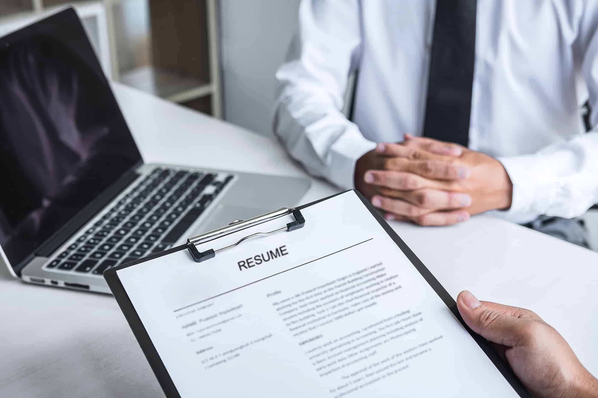Two men are discussing a resume and a laptop.