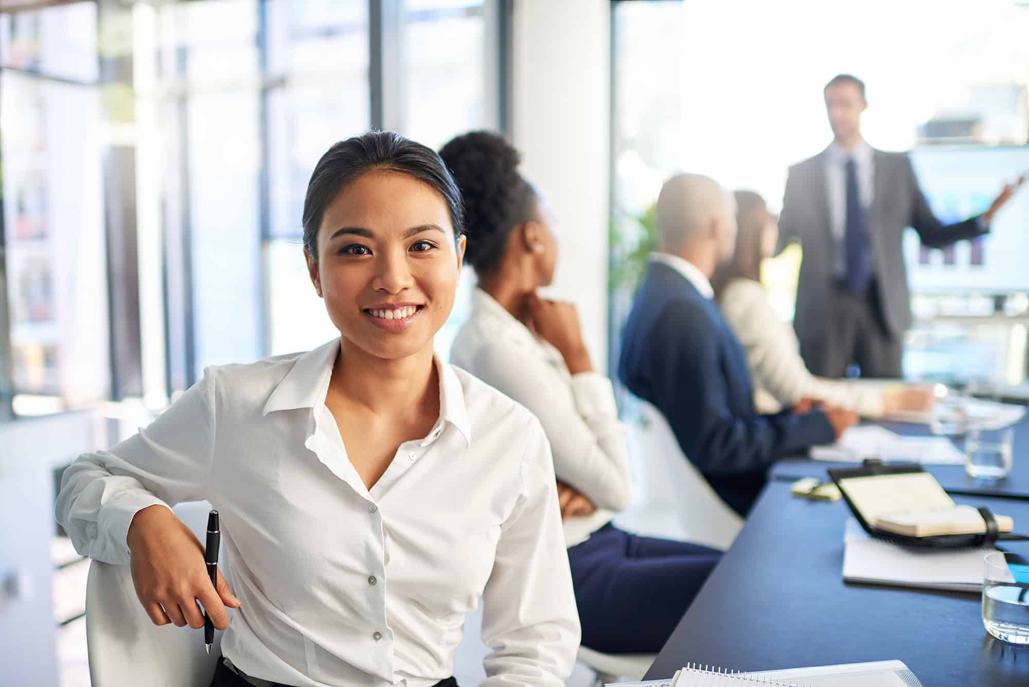 A confident community management associate in a professional office setting with colleagues in the background.