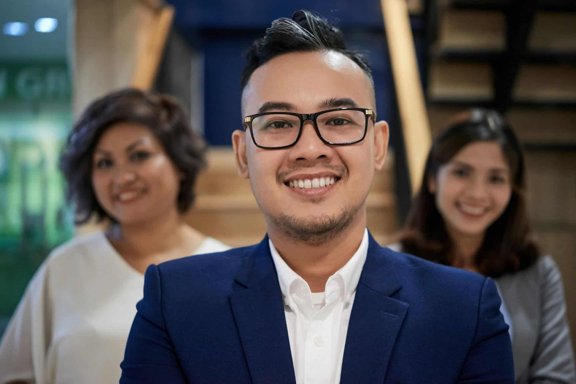 A property manager in a suit smiling confidently with colleagues behind him.